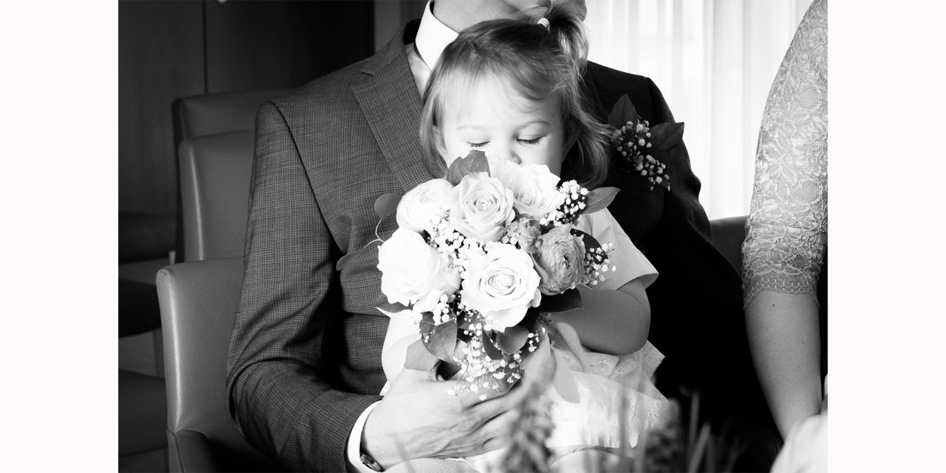Standesamt Hochzeit Kerpen Ein Kind hält einen Blumenstrauß und sitzt auf dem Schoß eines Erwachsenen.