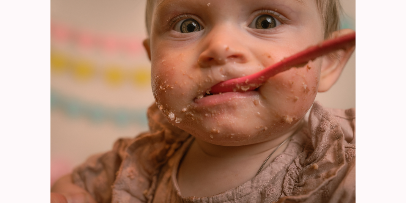 Ein Kleinkind mit schmutzigem Gesicht, das mit einem Löffel isst.