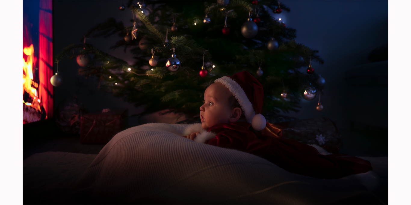 Ein Kind in einem Weihnachtspullover mit einer Weihnachtsmütze liegt neben einem Baum.