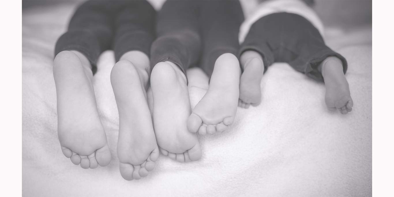 Füße von drei Personen liegen nebeneinander auf einem Bett.