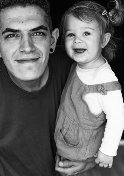 Ein lächelnder Mann hält ein kleines Mädchen in einem Kleidchen in den Armen beim Familienshooting in Kerpen