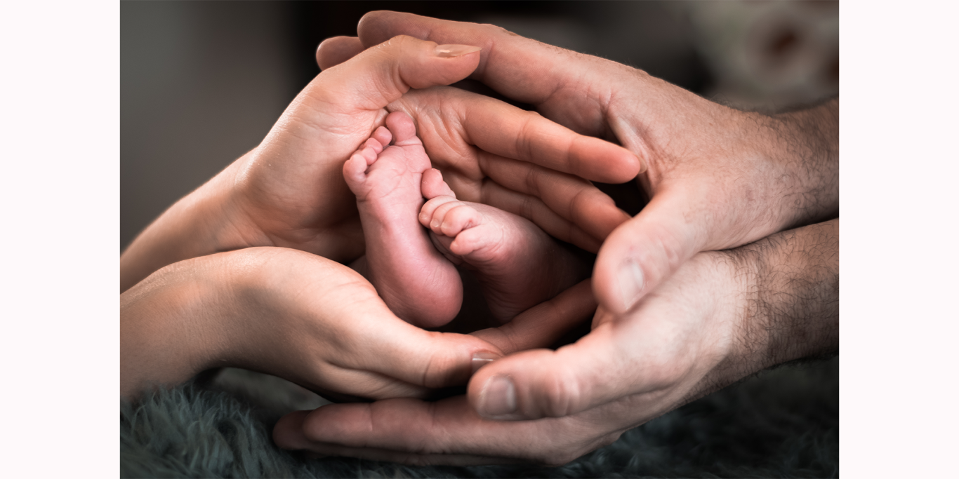 Hände eines Erwachsenen und eines Kindes halten den Fuß eines Neugeborenen sanft.