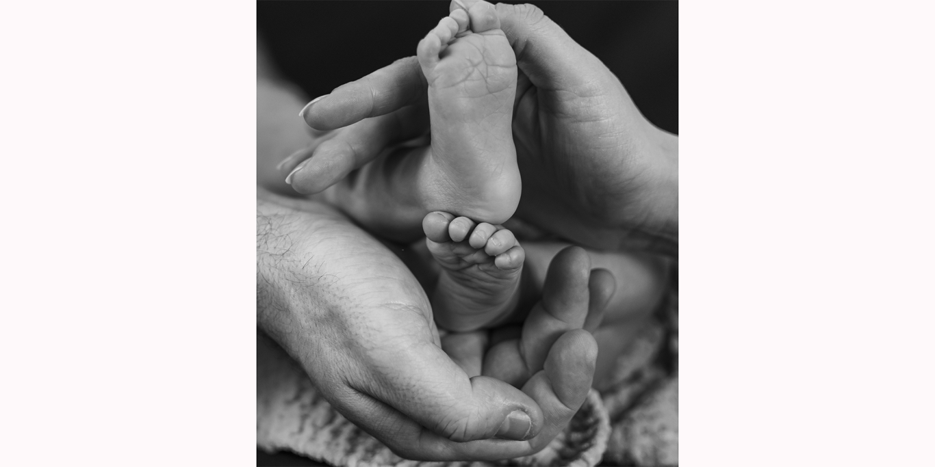 Hände halten den Fuß eines Neugeborenen mit sichtbaren Zehen.