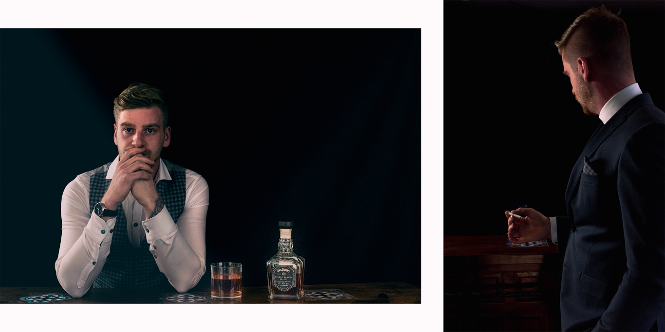 Ein Mann in formeller Kleidung sitzt an einer Bar mit zwei Gläsern Whiskey.