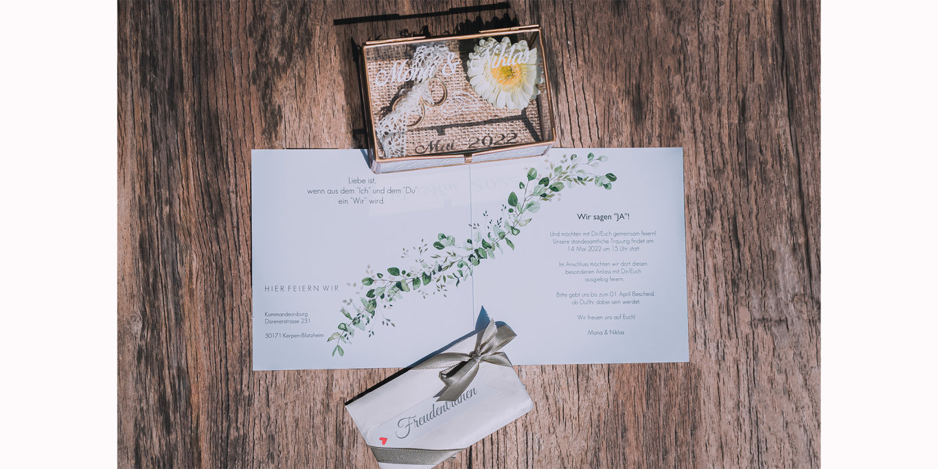 Flat lay Hochzeit Ein Tischarrangement mit Menü, Pflanzen und einer Holzbox.