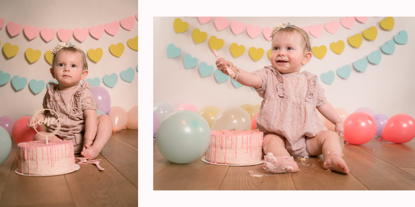 Ein kleines Kind sitzt neben einer rosa Torte, umgeben von Luftballons und Herzgirlanden.