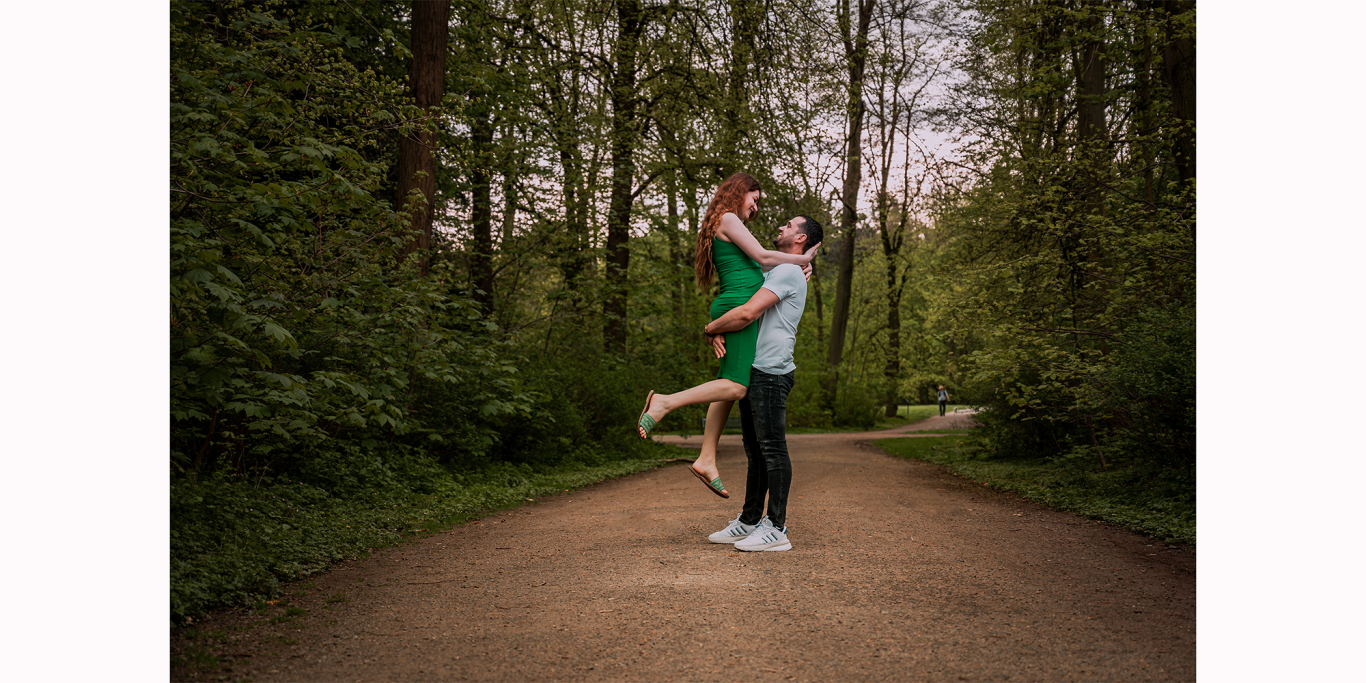 Paarshooting Köln Ein Paar steht auf einem Waldweg, der Mann hebt die Frau in einem grünen Kleid hoch.