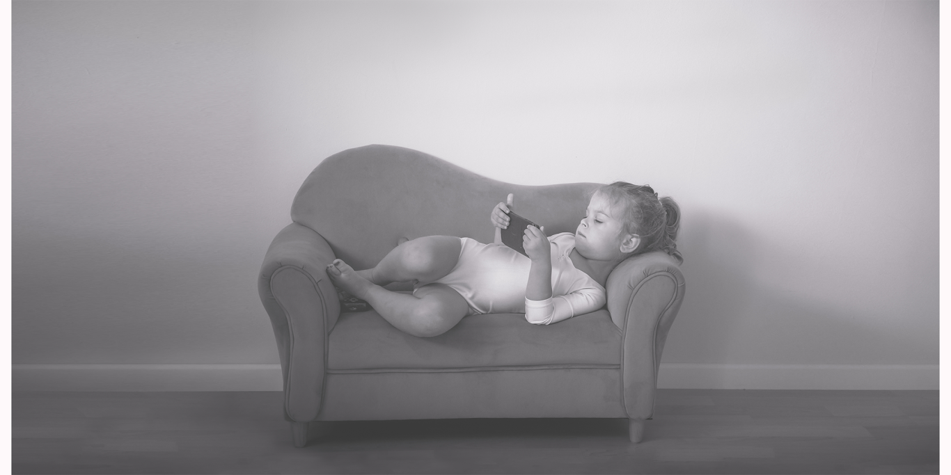 Familienshooting in Kerpen " Kleine Pause" Ein kleines Kind liegt entspannt auf einem Sofa und schaut auf ein Smartphone.